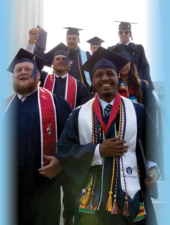 group of students in graduation attire walking through the columns