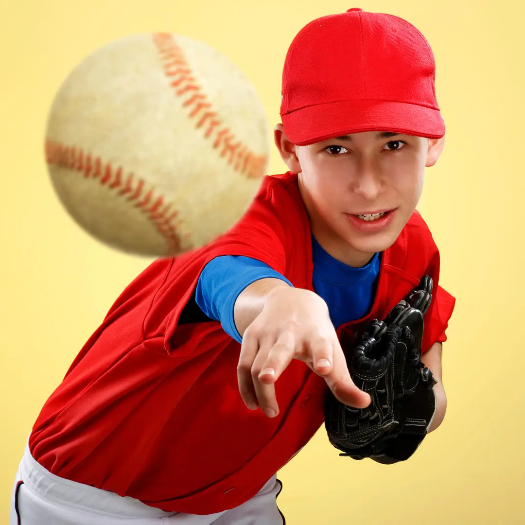A young baseball player in a red jersey and matching cap pitching a baseball directly toward the camera against a bright yellow background.