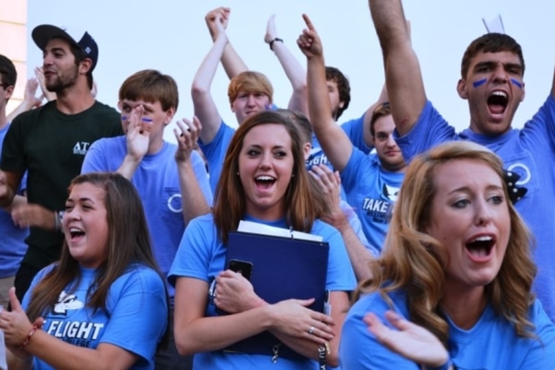 A crowd of Westminster College students in blue spiritwear cheer at a football game